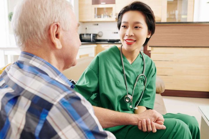A female nurse in green scrubs holding a patient's hand as a symbol of beneficence in nursing.