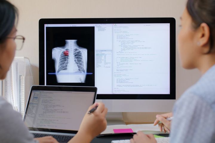 Health informatics professionals look at data on a screen.