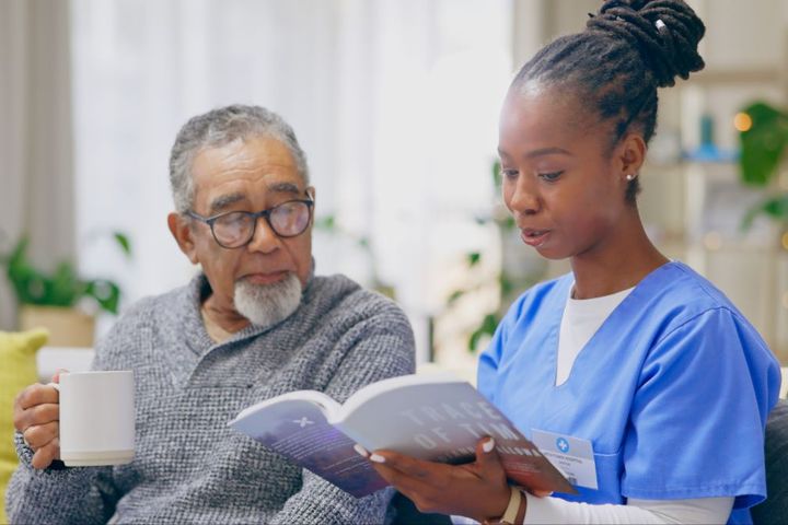 A hospice nurse reads a book to one of her patients.