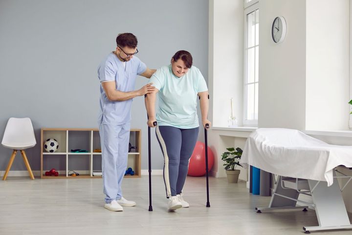 A medical professional helps one of his patients walk during a physical therapy session.