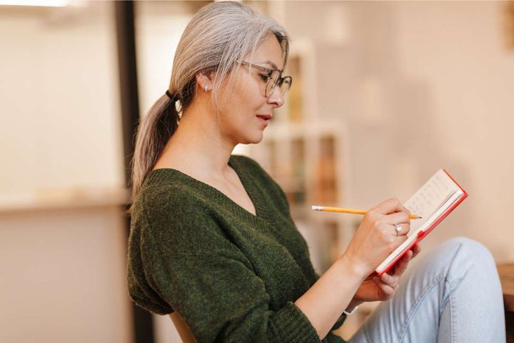 Woman with gray ponytail sitting and journaling after her nursing shift.