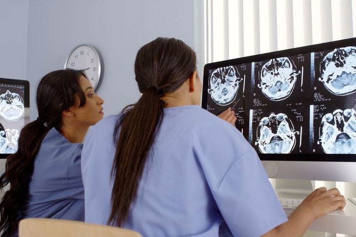 A nuclear med tech and a nurse look at brain scan images.