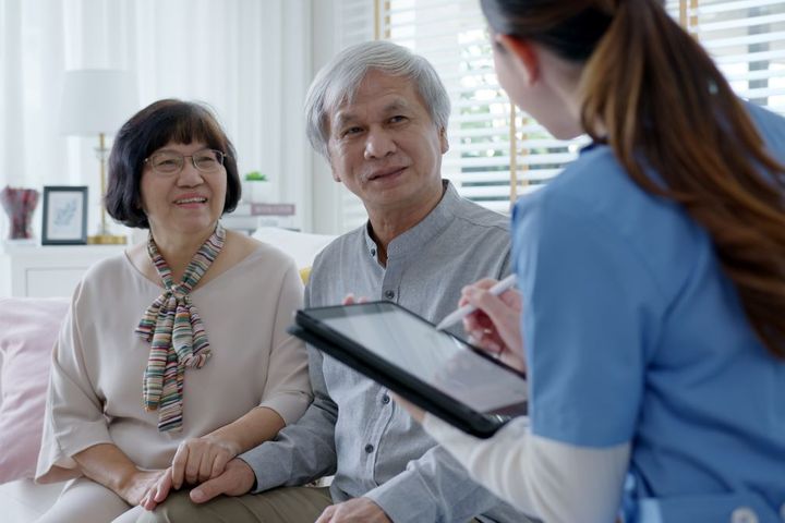A nurse takes notes as she talks with an elderly couple at an assisted living facility.