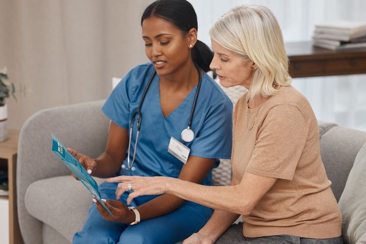 An RN sits and shows something on her tablet to a patient.