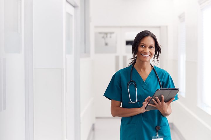 Float pool nurse with tablet smiling in hospital hallway.