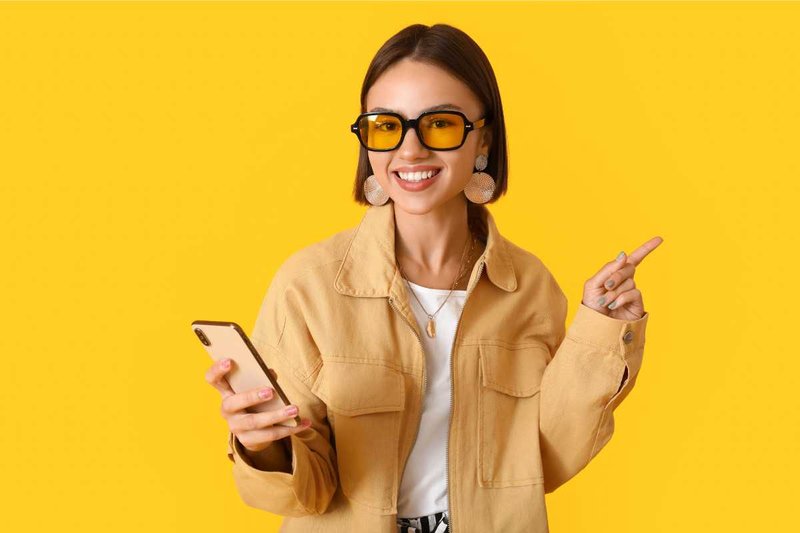 Woman on a yellow background wearing blue-light-blocking eyeglasses.