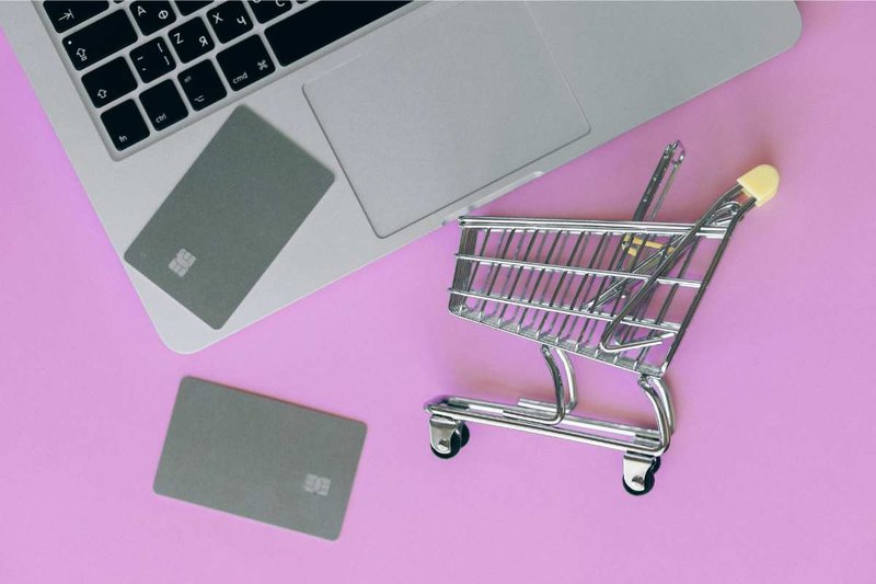 Two gift cards, a tiny shopping cart, and a laptop on a purple background.