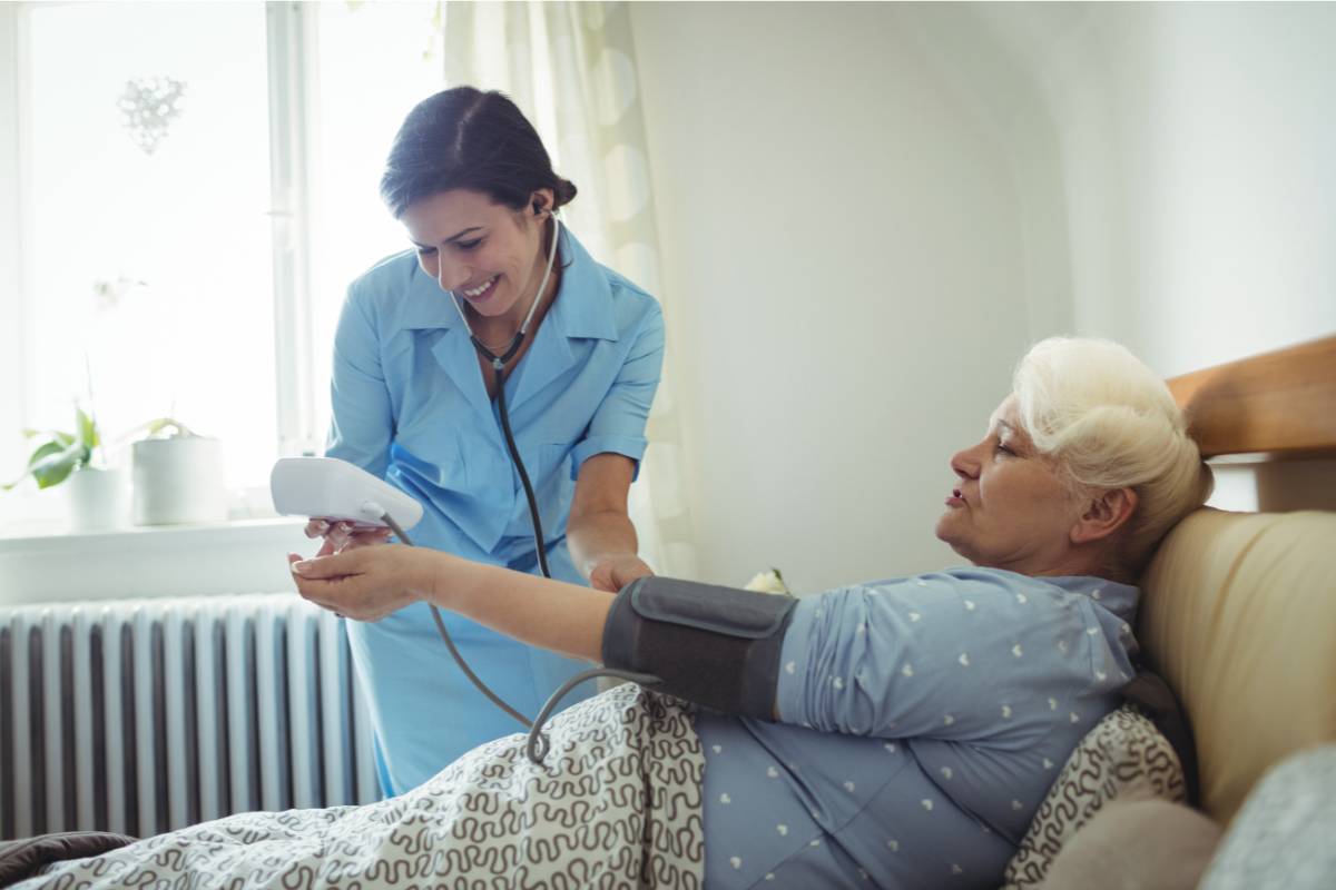 A nurse with ACHPN certification helps a patient in a hospital bed.