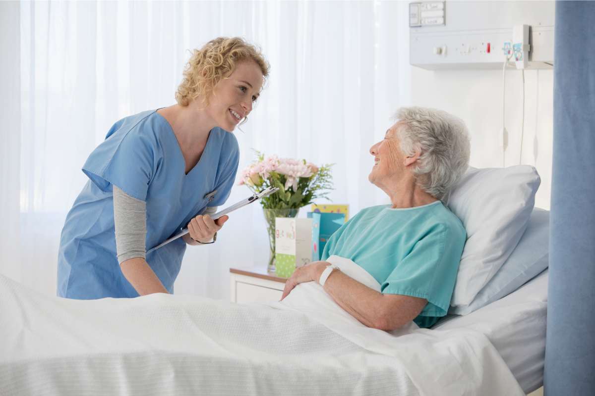 Nurse listening to a hospital-bed-bound elder woman.