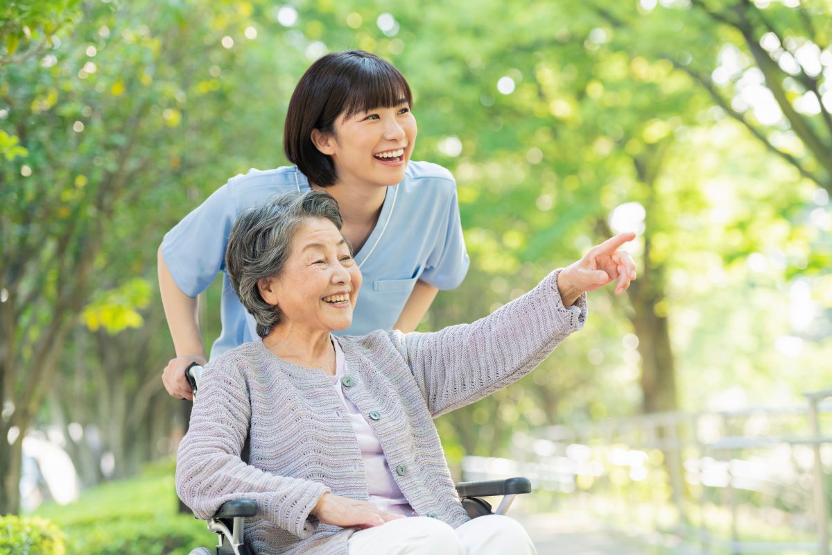 Certified nursing assistant performing her job description by pushing a resident in a wheelchair outdoors