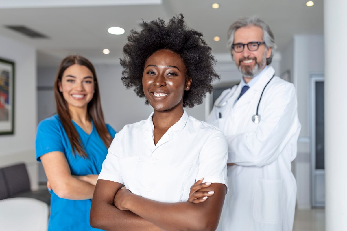 A nurse and two physicians stand and smile at the camera.