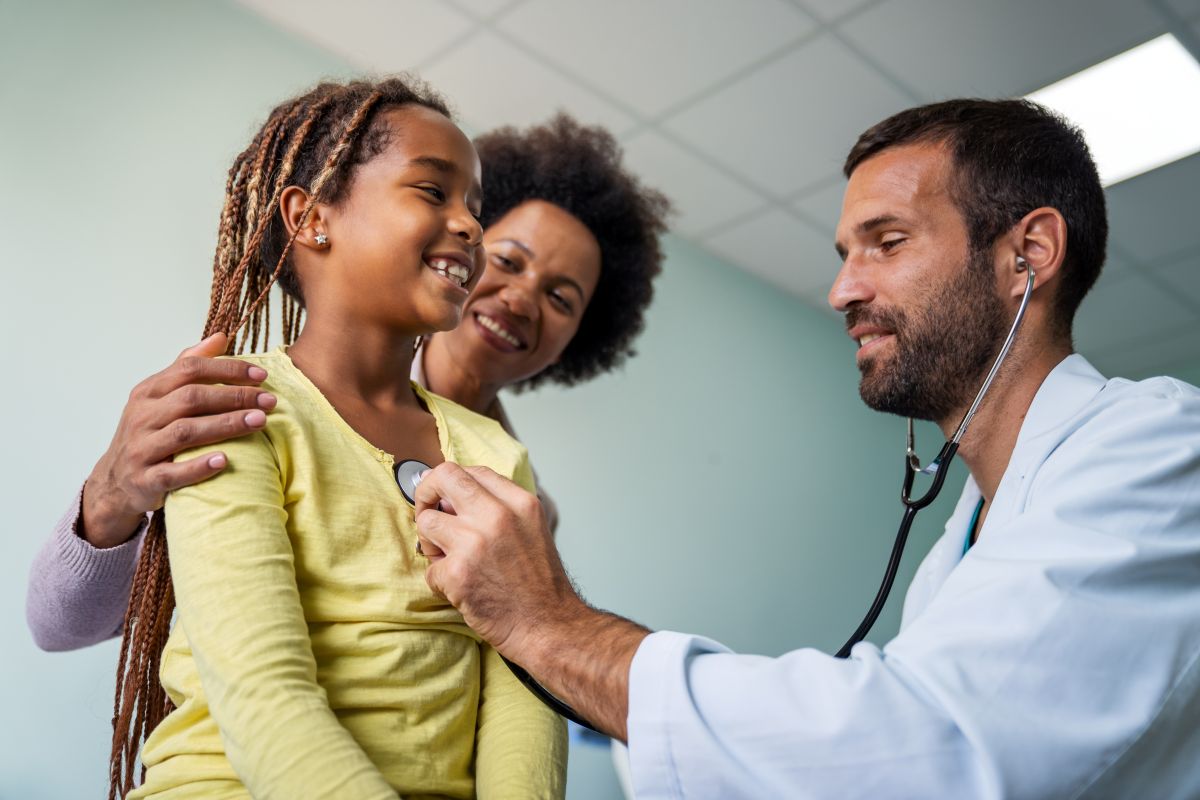 A family nurse practitioner checks a young girl's heartbeat as her mom watches on.