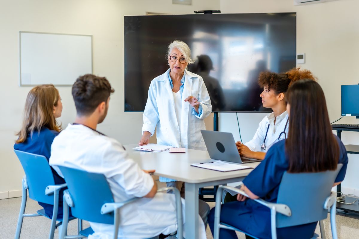 A nurse mentor teaches a group of younger nurses.