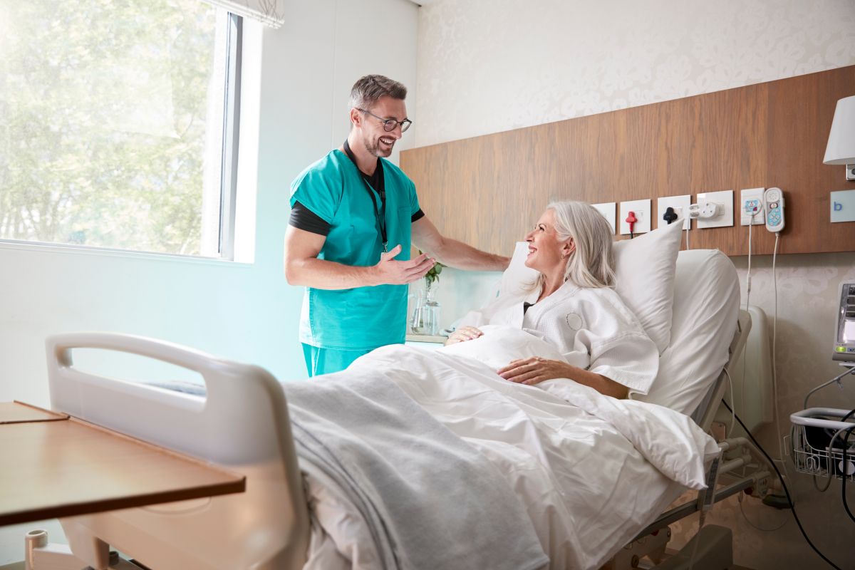 A nurse meets one of his patients, who is reclining in a hospital bed.
