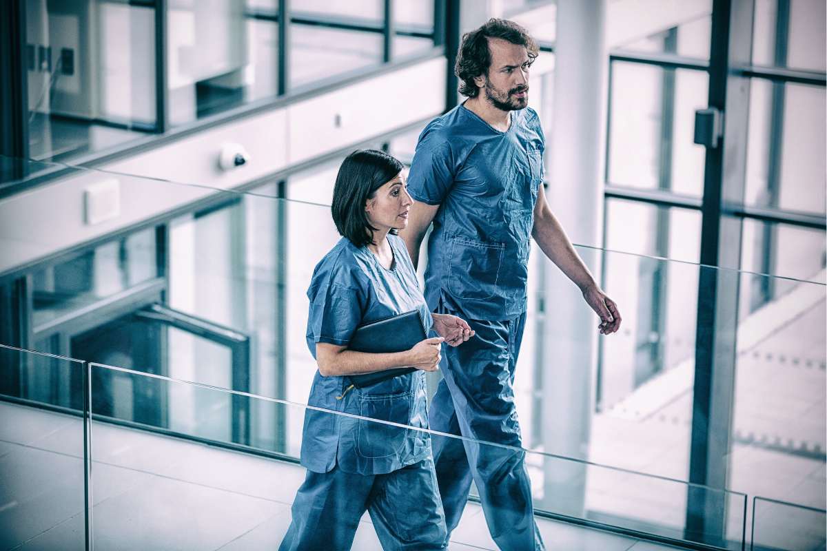 Male and female nurses in scrubs walking through hospital.