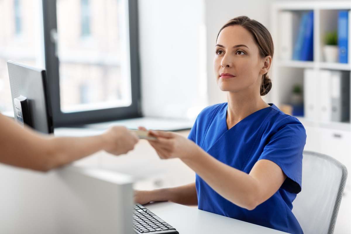 Female medical scribe in blue scrubs behind the desk at an ambulatory clinic.