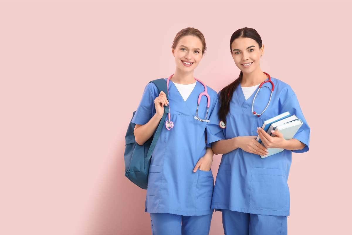 Two young women in blue scrubs holding books learning how to become a nurse after high school.