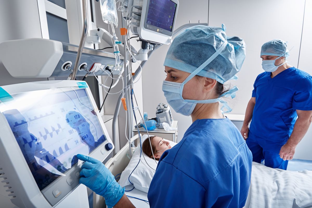 Two ICU nurses check the patient and monitors after a procedure.