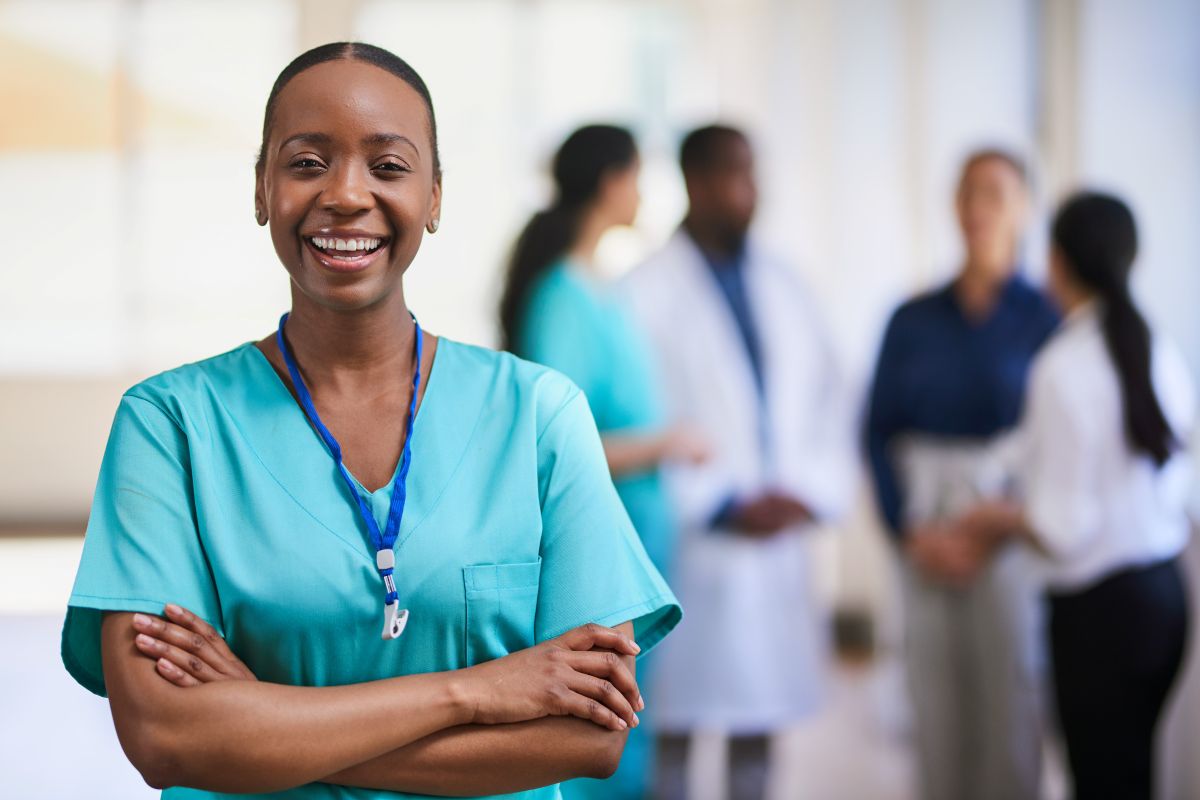 A nurse stands in the foreground, smiling at the camera.
