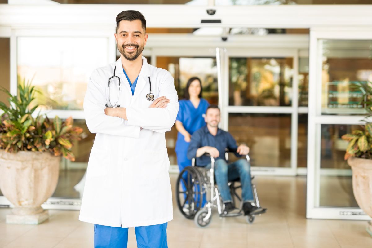 A physician stands outside of a hospital entrance.