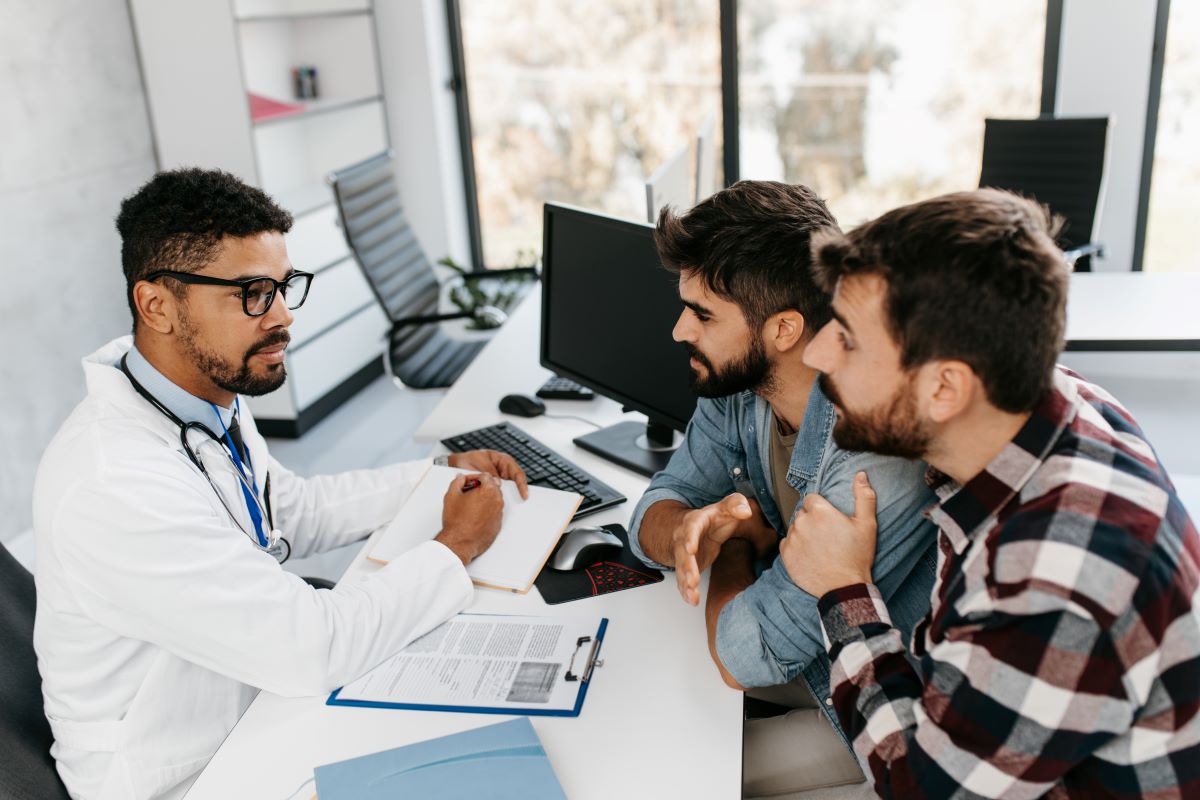 A physician consults with a man and his partner in an office.