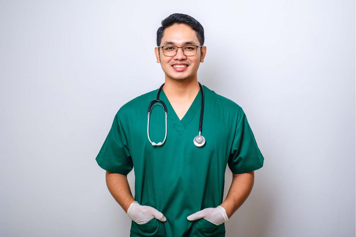 Smiling male nurse in green scrubs with a stethoscope around his neck.