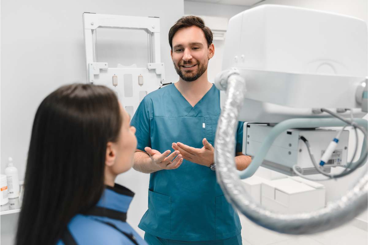 Male medical assistant in blue scrubs with a diagnostic tool and patient.