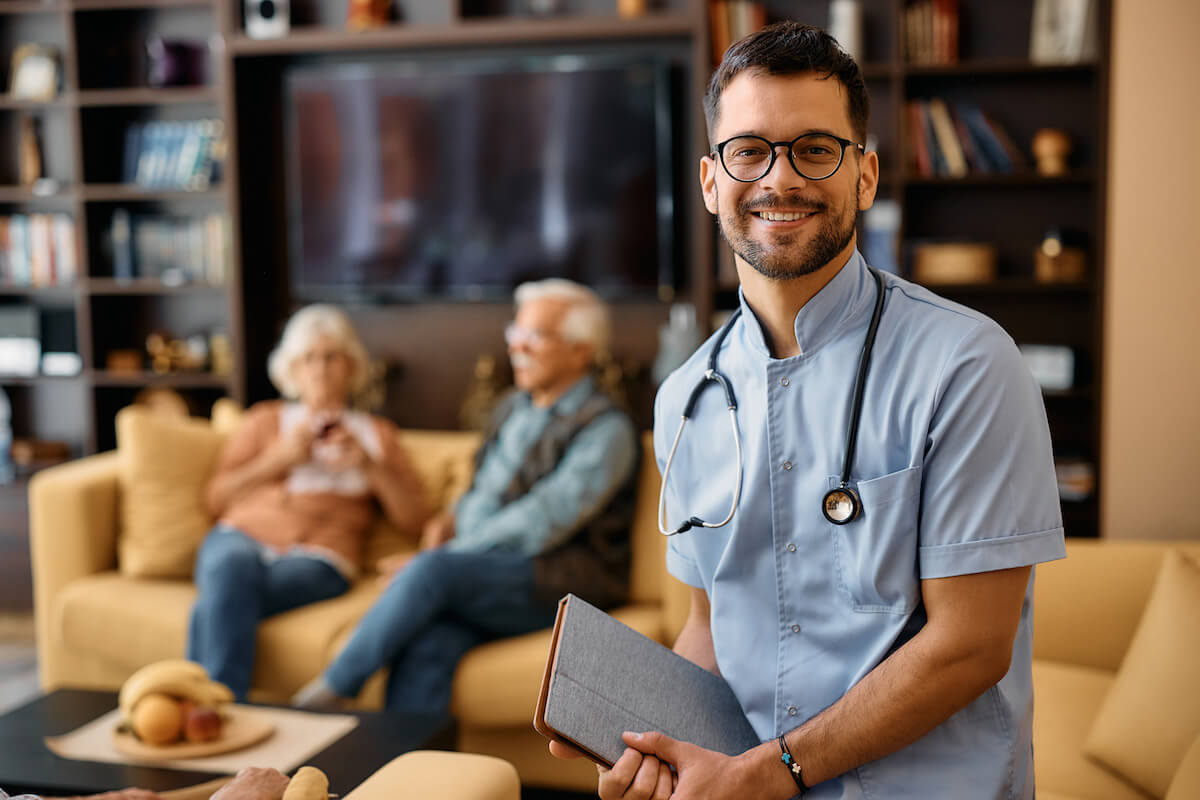 Male nurse with beard and glasses smiling in an assisted living facility.