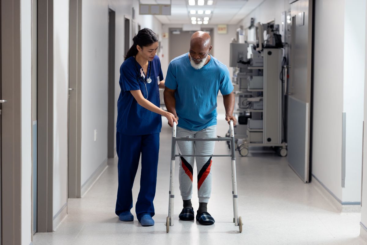 A nurse helps one of her patients walk down the hallway, as he learns how to use a walker.