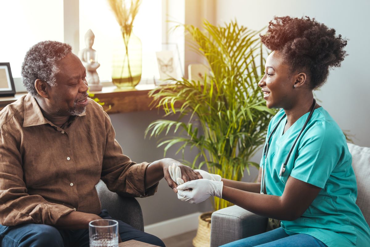 A nurse holds the hand of a patient with dementia as she talks with him.