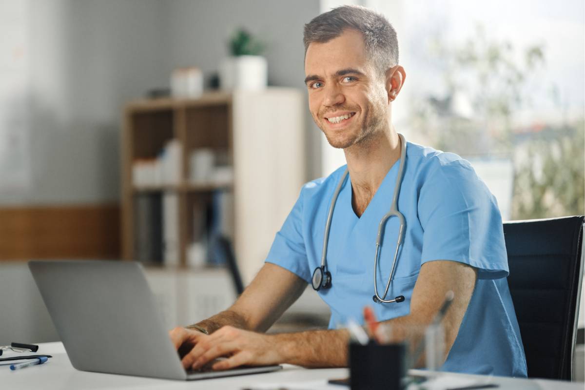 A man in blue scrubs writes his nursing resume summary.