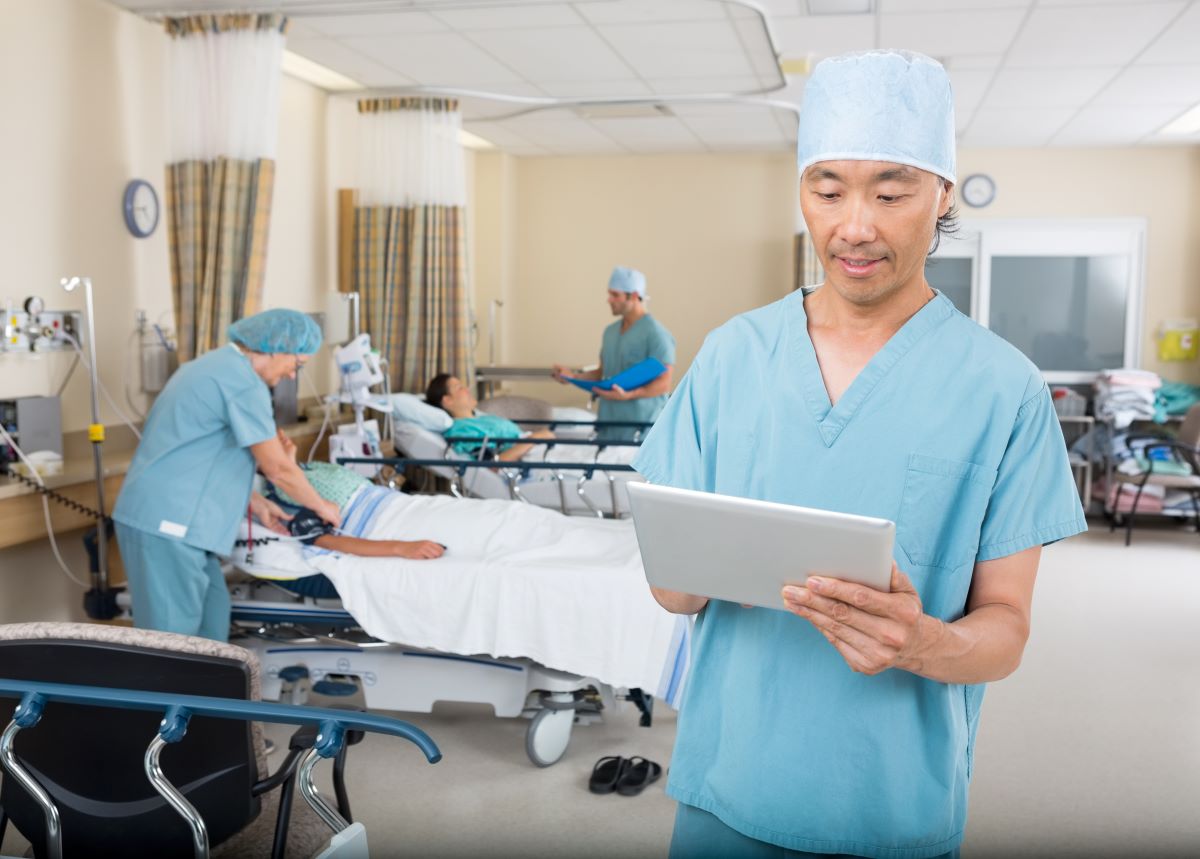 A PACU nurse checks his tablet next to a patient's bed.