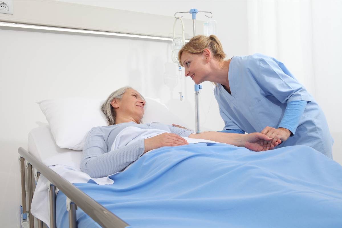 A palliative care nurse practitioner greets a patient in a hospital room.
