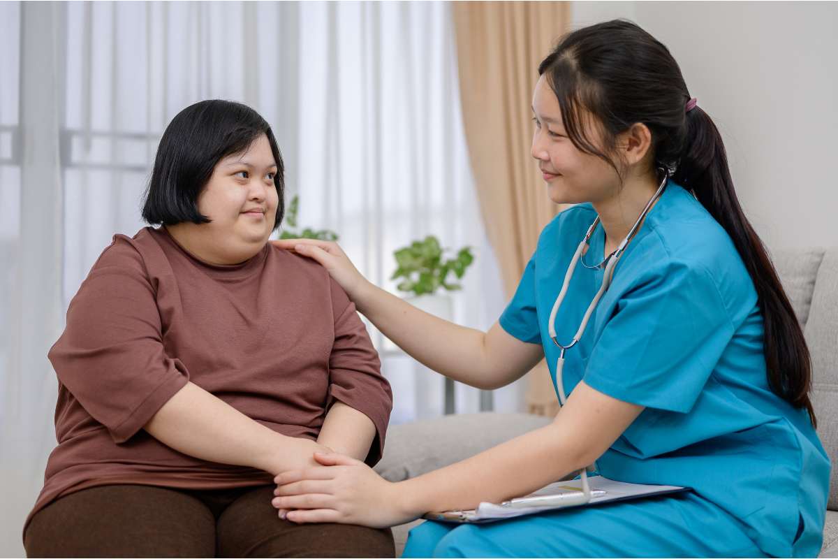 A parish nurse sitting with patient, placing her hand on the patient's shoulder.