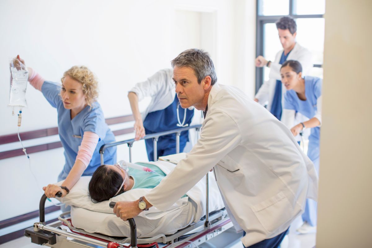 A patient transporter helps move a patient on a stretcher to another room in the hospital.