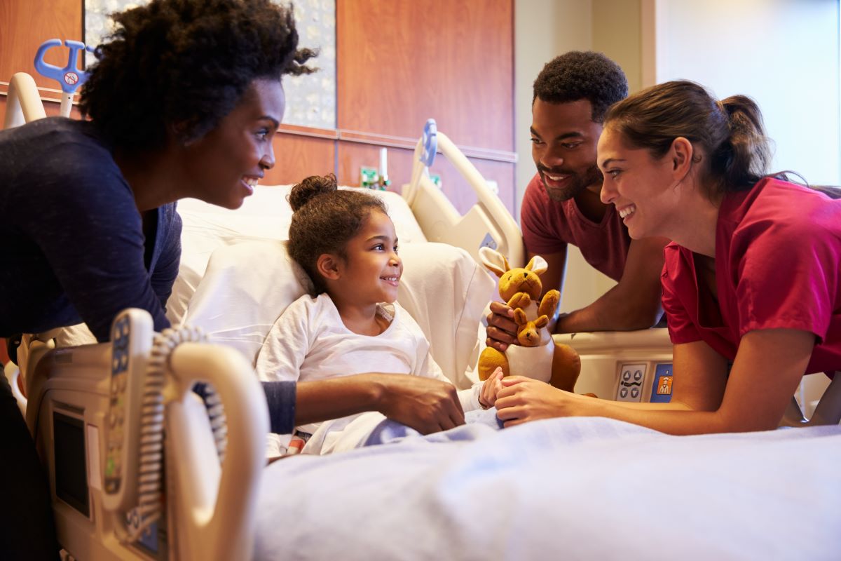 Pediatric nurses cheer up a child patient who's in a hospital bed, along with the child's father.