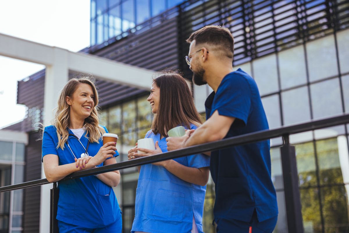 Three nurses on break enjoy coffee outside of a hospital.