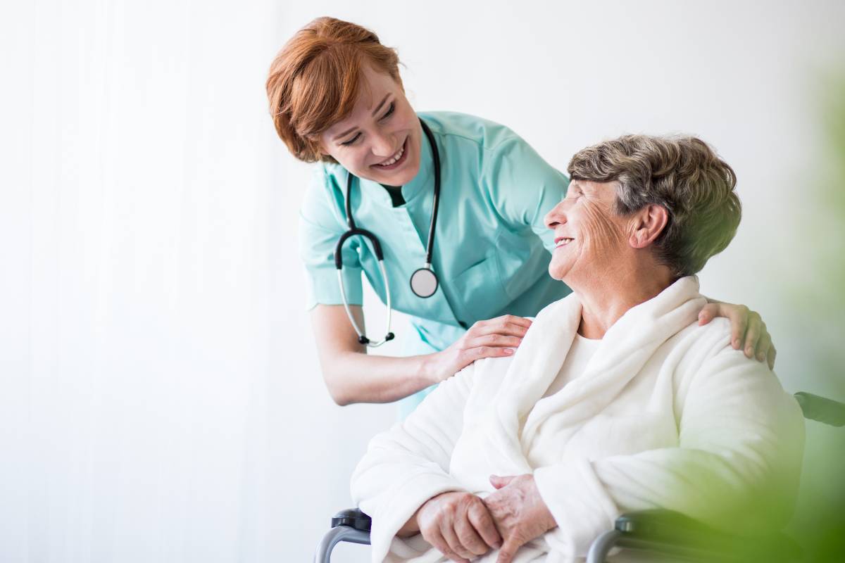 A nurse in rheumatology nursing assists a patient in a wheelchair.