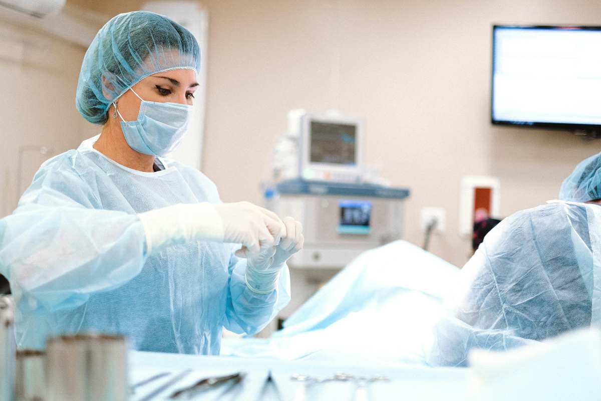 A surgical tech in the operating room, wearing full scrubs and tending to a patient.