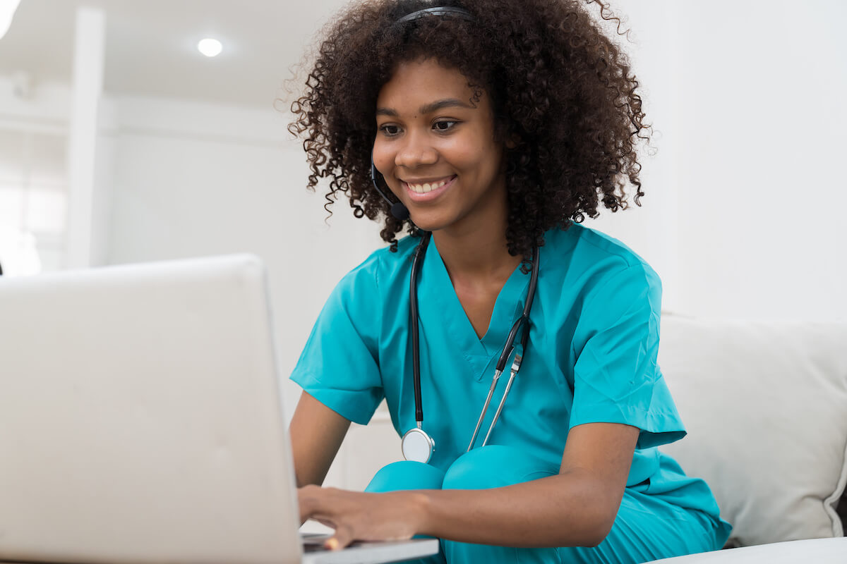 African American travel nurse writing her resume on a laptop.