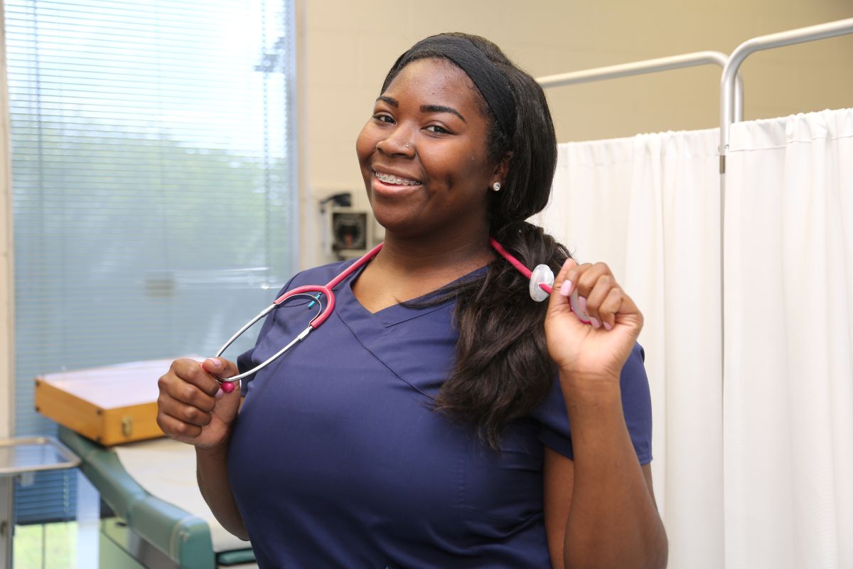 A urology nurse stands and smiles at the camera while standing in a patient's room.