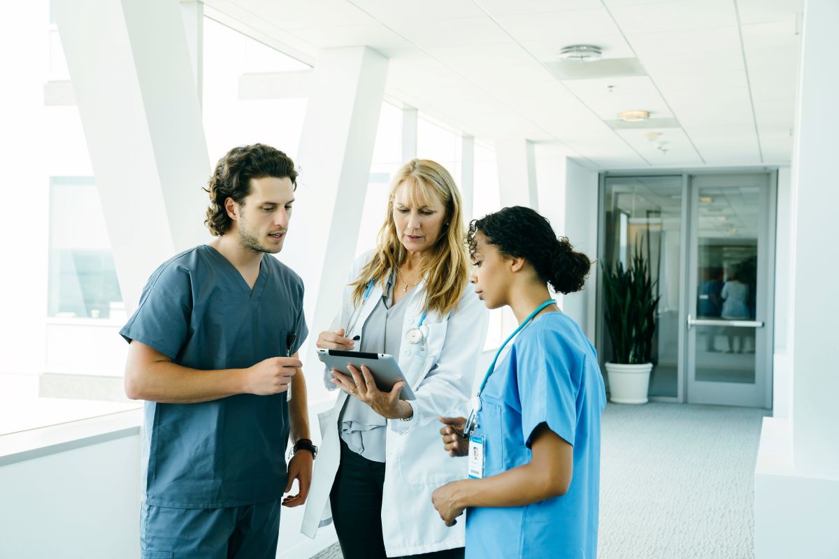 A doctor and two nurses discuss a patient while looking at their electronic records on a tablet.