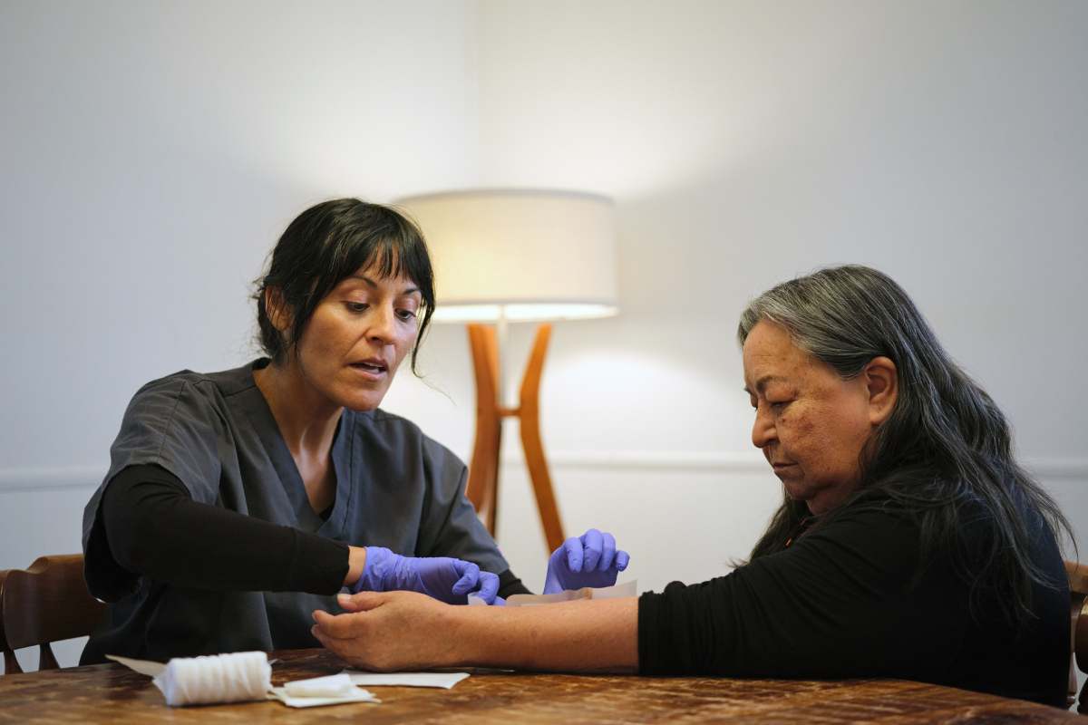 Female wound care nurse practitioner changing a bandage dressing on an older Native American woman at her home.